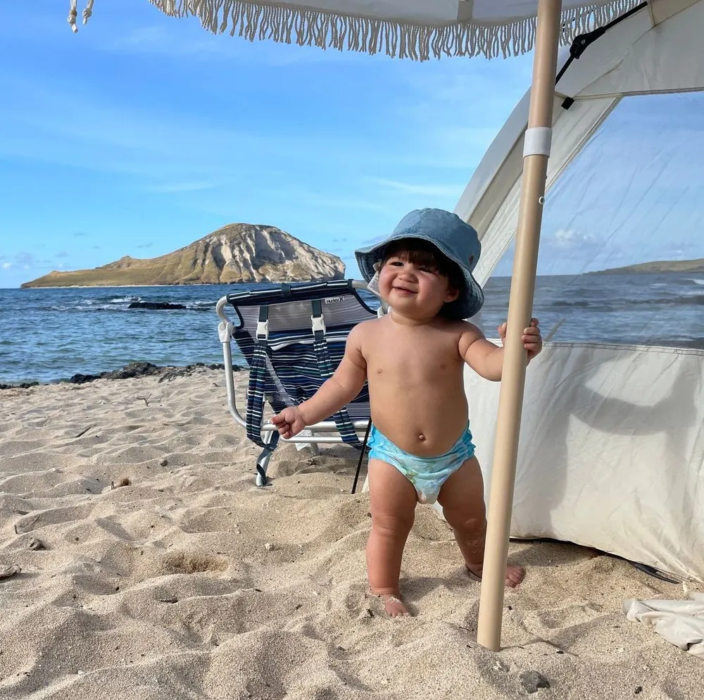 A smiling toddler in a sun hat on a windward Oʻahu beach